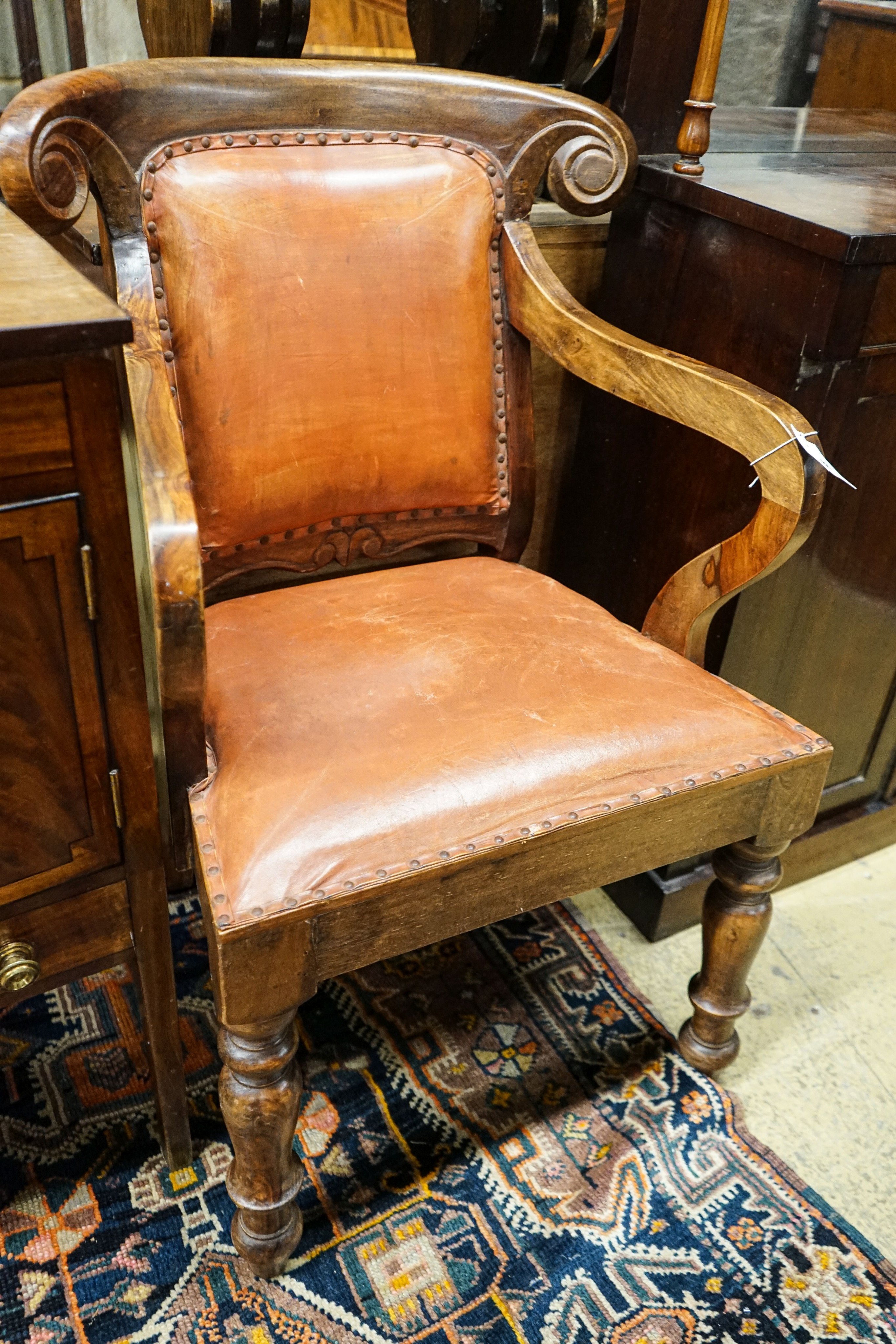 A pair of Victorian style hardwood elbow chairs with faded red leather upholstery, width 55cm, depth 45cm, height 92cm